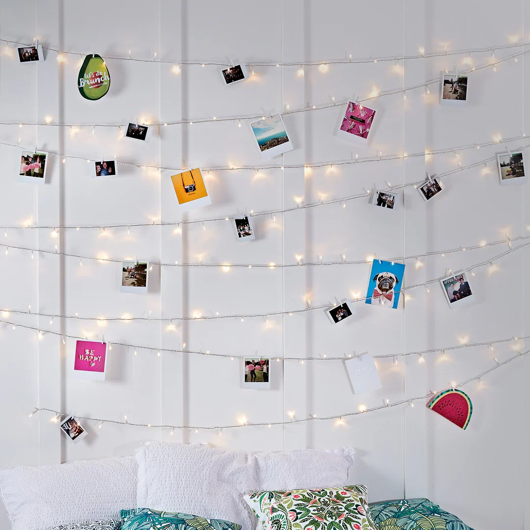 Lichtgirlanden mit Fotos und bunten Karten an einer weißen Wand dekoriert.